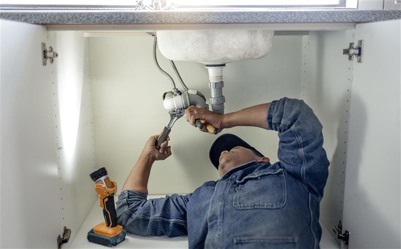Plumber repairing pipes beneath a bathroom sink in Holiday