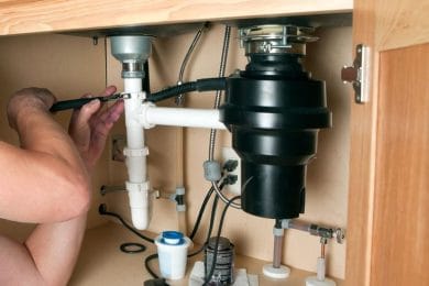 Plumber repairing a garbage disposal beneath a kitchen sink in Holiday