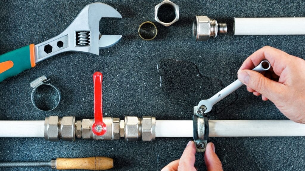 Plumber repairing a pipe valve with an adjustable wrench in Holiday