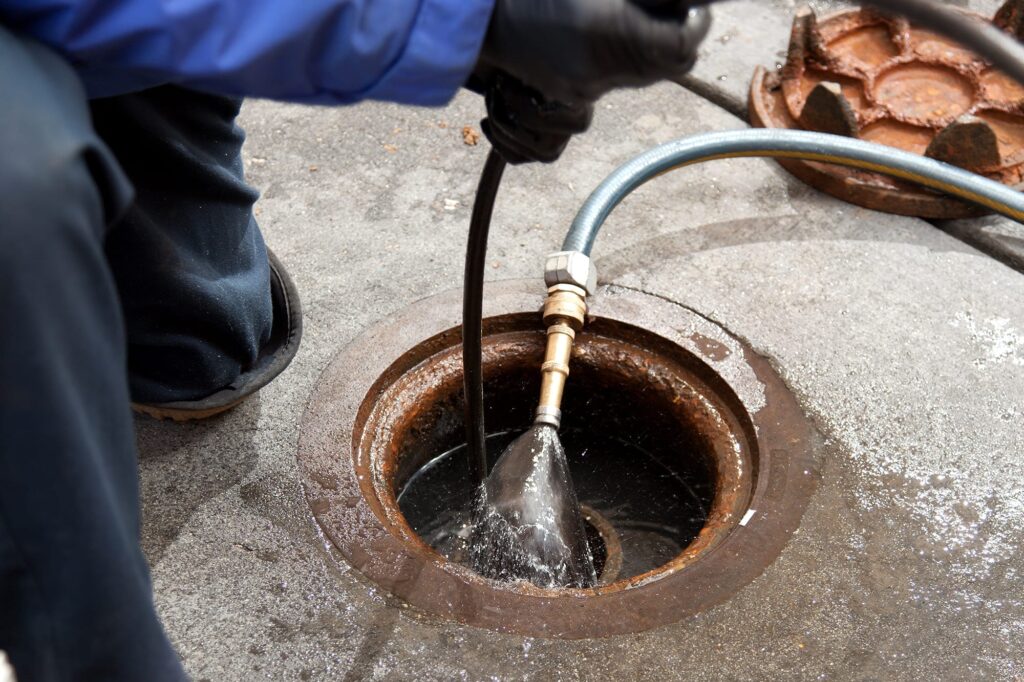 Plumber hydro jetting a sewer line through a manhole in Holiday