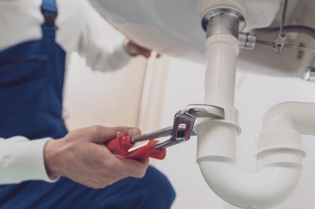 Plumber repairing a white drain pipe beneath a sink in Holiday
