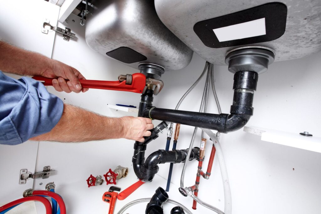 Plumber repairing drain pipes beneath a kitchen sink in Holiday
